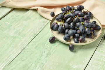 Plate with sweet black grapes on green wooden background