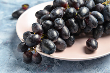 Plate with sweet black grapes on blue background