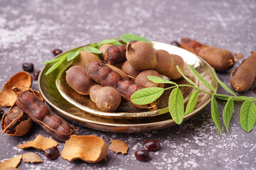 Plates of tasty tamarinds, leaves and seeds on grey background