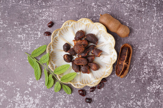 Plate of tasty tamarinds, seeds and leaf on grey background