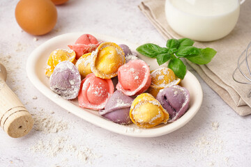 Plate with colorful raw dumplings and basil on white background