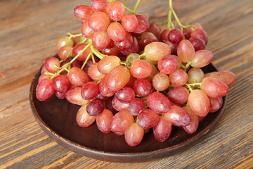 Plate with tasty ripe grapes on wooden background