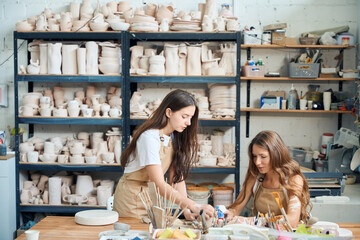 Female teaching young woman to work with clay making ceramic plate
