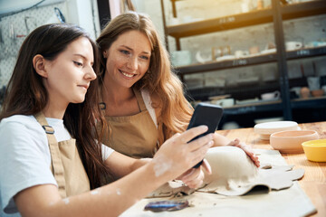 Women using smartphone while working with clay in pottery workshop