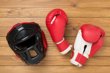 Boxing helmet and gloves on wooden background, top view.