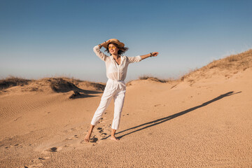 stylish beautiful carefree happy woman walking in desert sand dressed in white outfit
