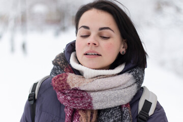 Young smiling beautiful woman wearing scarf outdoors during snowfall