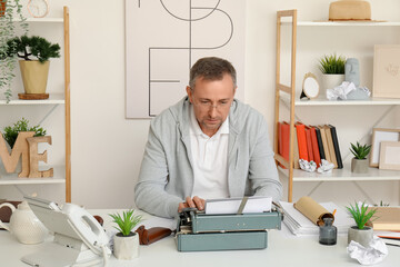Mature man with scroll and paper sheets typing on vintage typewriter at table in office