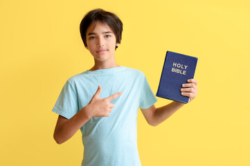 Little boy pointing at Bible on yellow background