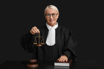 Mature female judge with scales of justice and book at table on black background