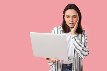 Confused young woman with laptop on pink background