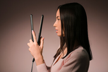 Obraz premium Beautiful young woman with hair straightener on pink background