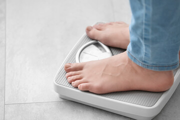 Young woman standing on scales at home, closeup. Weight loss concept