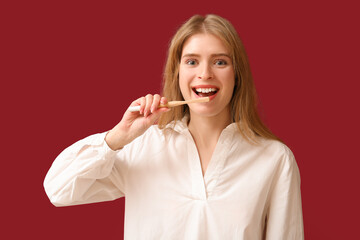 Young woman brushing her teeth on red background