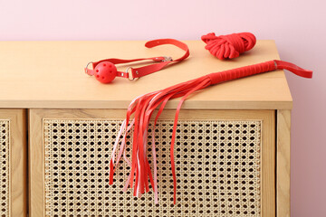 Red sex toys on chest of drawers near beige wall in room