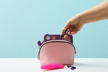 Female hand with nipple clamp from sex shop and cosmetic products on light background
