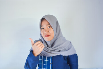 Close up photo of beautiful cheerful Asian Muslim woman, with hand gesture pointing at empty space isolated on pink background