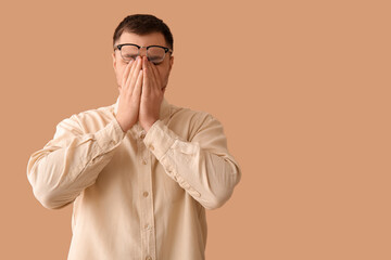 Tired young man with eyeglasses on beige background