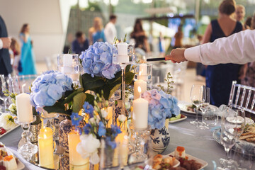 Waiters men in uniform lights candles on the festive table. Flowers and candles on wedding table. 