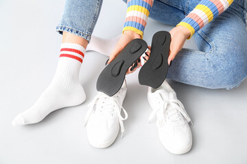 Young woman sitting and putting orthopedic insoles in sneakers isolated on white background
