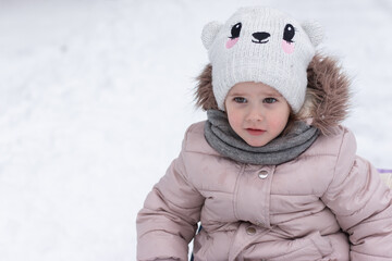 Little beautiful girl in a knitted hat, glasses and warm clothes outdoors in winter. Children's games in the snow