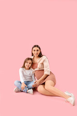 Little girl with her pregnant mother hugging on pink background