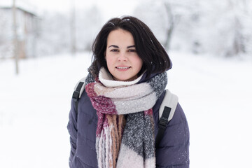 Young smiling beautiful woman wearing scarf outdoors during snowfall