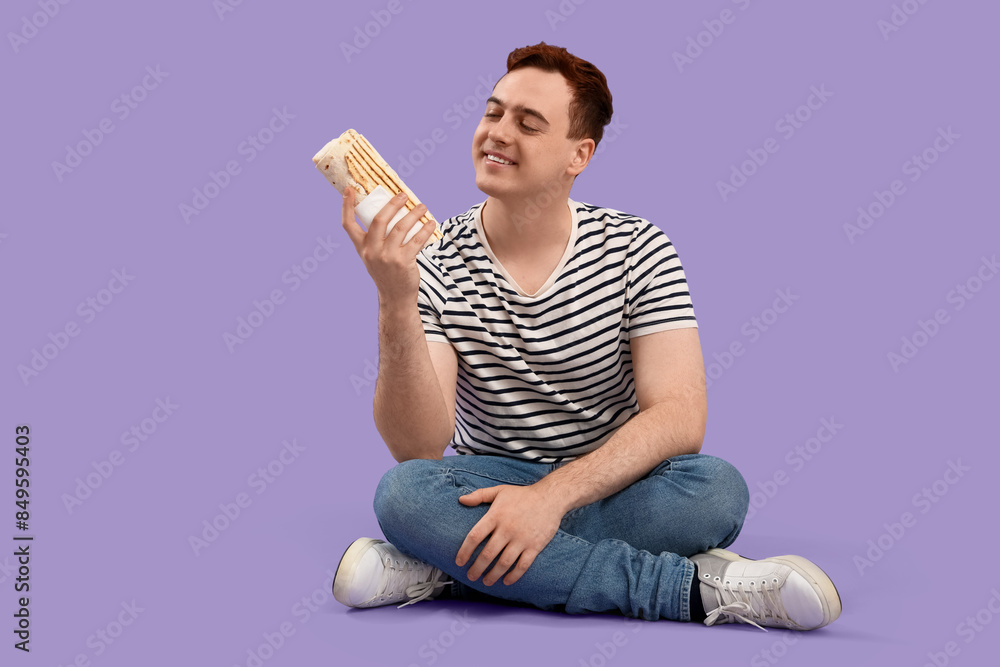 Sticker Young man sitting and holding doner kebab on purple background