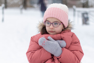 Little beautiful girl in a knitted hat, glasses and warm clothes outdoors in winter. Children's...