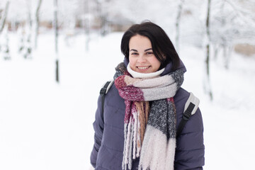 Young smiling beautiful woman wearing scarf outdoors during snowfall