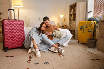 Young couple of tourists using mobile phone in hotel room at night