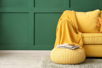 Yellow pouf with magazines and sofa near green wall in living room