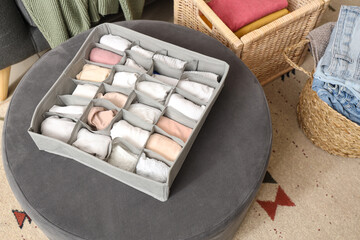 Organizer with clean clothes on pouf in room