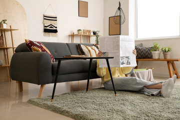Young woman reading newspaper on floor in living room
