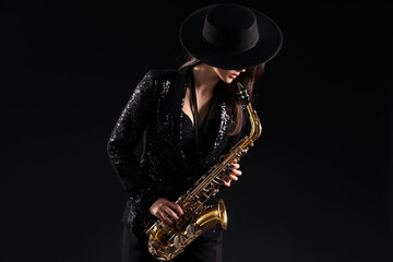 Naklejka premium Beautiful young woman playing saxophone on dark background