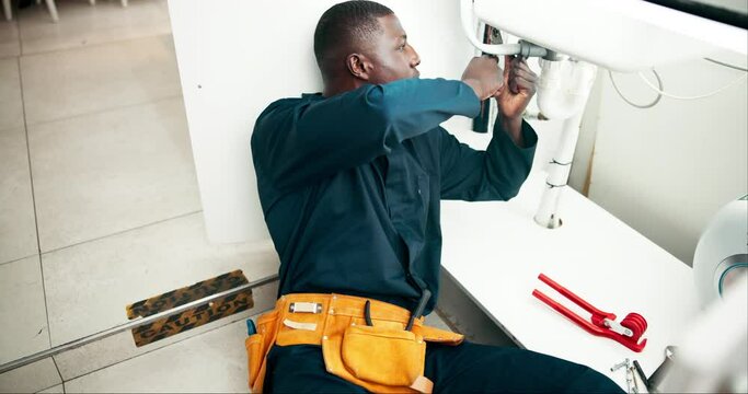 Black man, plumbing and pipe with repair for fix, leak or sink in maintenance or service at home. Young African, male person or plumber working on faucet, basin or water leakage in kitchen at house