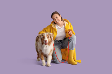 Pretty young woman in raincoat with cute Australian Shepherd dog on lilac background
