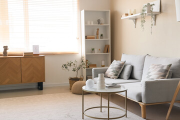 Stylish interior of light living room with cozy couch, coffee table and shelving unit
