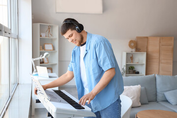 Young bearded man in headphones playing synthesizer at home
