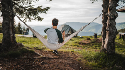Young boy sit in a hammock and drink coffee on the mountain