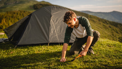 Young adult caucasian boy mounted tent with hatchet on the mountain