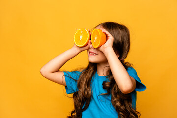 Close up studio portrait of child smiling, holding halves of citrus fruit oranges at her eyes on yellow background. Holiday, summer, fashion concept. Copy space