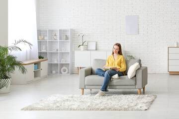 Young woman reading book on sofa in living room