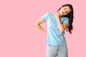 Beautiful young woman suffering from neck pain on pink background