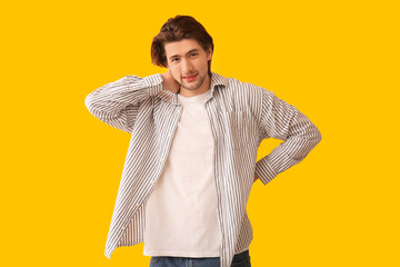 Handsome young man suffering from neck pain on yellow background