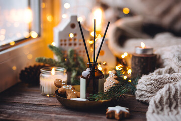 Xmas spirit, simple way to creating holiday atmosphere and festive mood at home on the window sill. Scented burning aromatic candles on wooden tray, liquid reed diffuser with sticks, fir tree branch