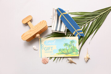 Composition with travel gift voucher, mini beach accessories and palm leaf on light background