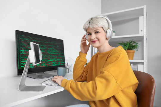 Female programmer with headphones and computer working in office