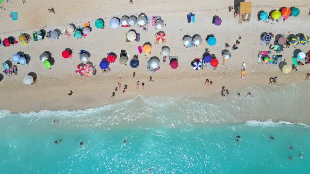 An aerial view of Porto Katsiki beach in Greece, showing the white sand, turquoise water, and colorful umbrellas lining the shore.