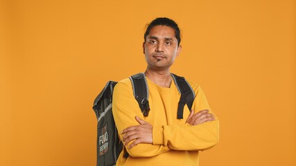 Portrait of upbeat indian man holding thermal backpack, isolated over studio background. Friendly cheerful person prepared to deliver takeaway food to customers, camera A